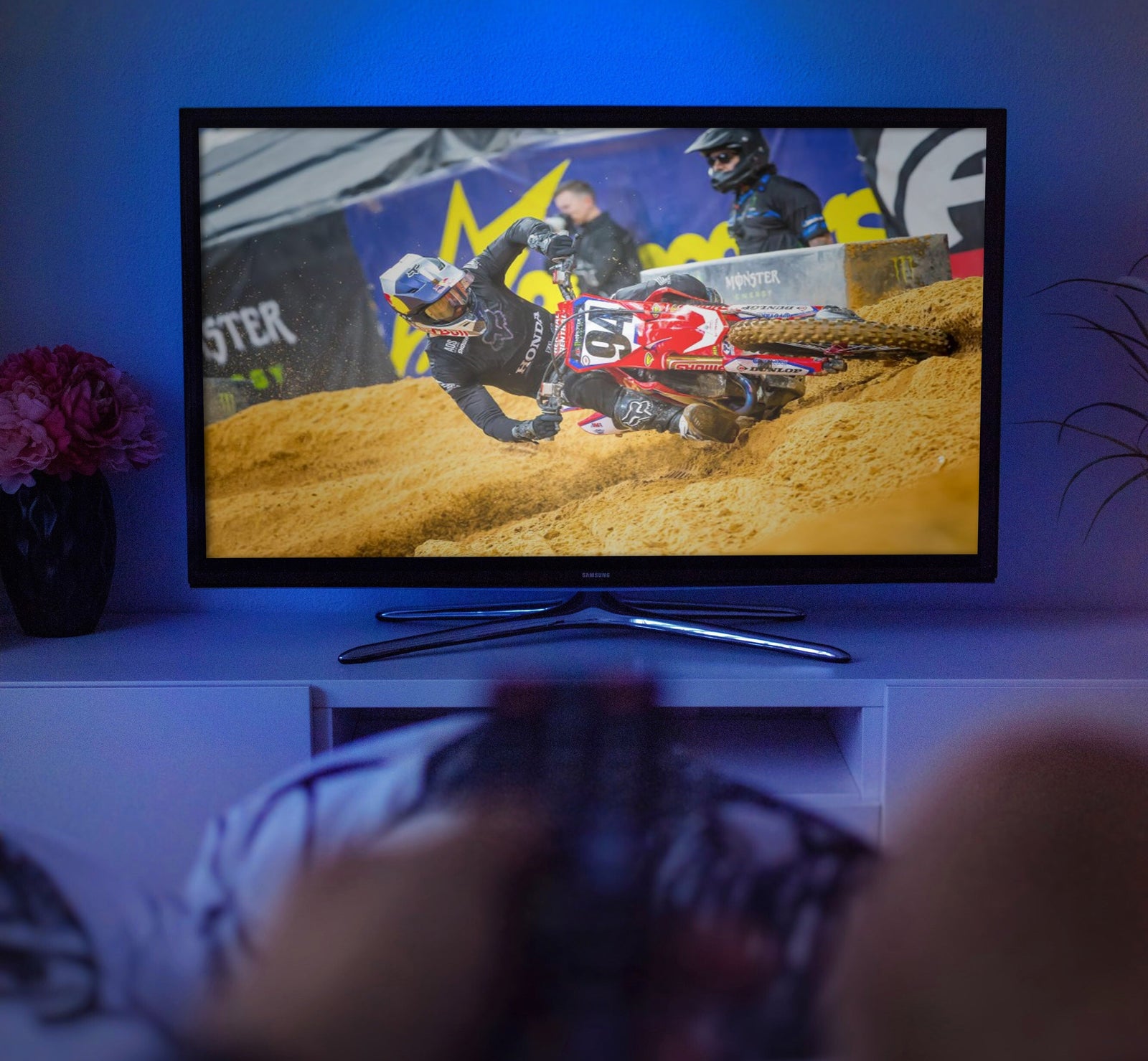 pov person watching tv. hand holding remote blurry at bottom. main image of a tv with motocross racing on screen.