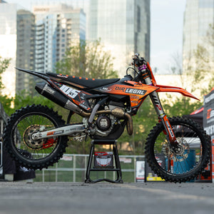 Orange-schwarzes Dirtbike auf einem Risk Racing F.F.S. Stand mit Stadtbild im Hintergrund